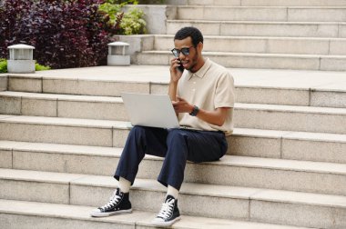 İş adamı merdivenlerde oturuyor ve şehirdeki bilgisayarda çalışıyor.