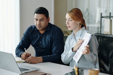 Genç kadın ve erkek iş stratejilerini tartışırken, iş birliği toplantısı sırasında ofis masasında birlikte belgeleri gözden geçiriyorlar.
