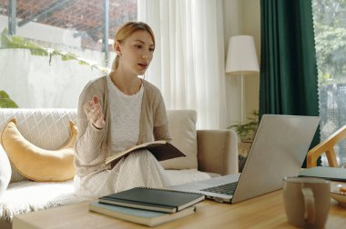Kanepede oturan bir kadın dizüstü bilgisayarla internetteki bir toplantıda kahve masasında oturuyor. Görünür yeşil perde ve rahat ortam sağlayan yastıklı parlak oda kurulumu