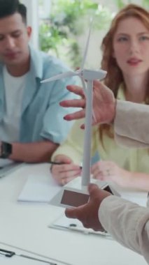 Mühendisin masasında oturan ve iş planı yazan ekibe rüzgar türbini modelini sunarken dikey çekimi