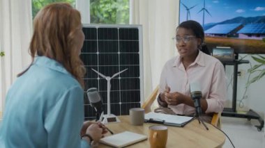 Genç Afrikalı Amerikalı mühendis ve Kafkasyalı gazetecinin ofisteki alternatif enerji üretiminde podcast yaparken orta boy çekimleri.