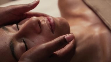 Gözleri kapalı genç bir kadının, güzellik salonundaki terapi sırasında yüz bölgelerine masaj yaparken yakın plan çekimleri.