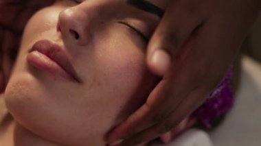 Oturum sırasında gözleri kapalı yatarken elmacık kemiği masajı yapmaktan hoşlanan genç bir kadının yüz görüntüsü.