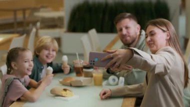 Kafkasyalı neşeli ebeveynlerin ve çocuklarının akıllı telefonlarıyla fotoğraf çekerken hafta sonları yemek alışveriş merkezinde oturup abur cubur yediklerini görmek.