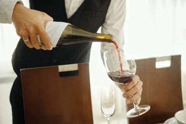 Şölen sırasında üniformalı garsonun elinde şişe tutarken ve şarap kadehlerine kırmızı şarap koyarken.