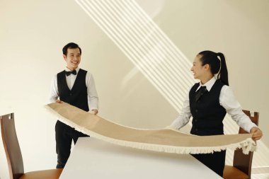 İki garsonun elinde dekor bezi var ve restorana gitmeden önce yemek masasına yayıyorlar.