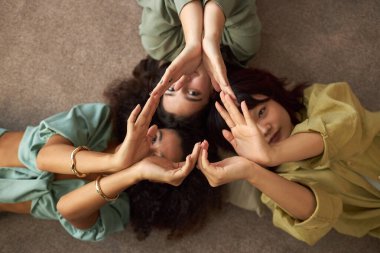 Üç etnik çeşitlilikte kızın oturma odasında yerde yatıp el kalbi yaparken tepeden tırnağa çekimleri.