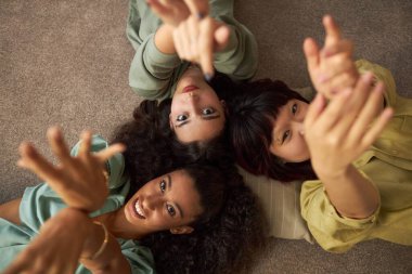 Yukarıdan bakıldığında, üç farklı etnik açıdan en iyi arkadaşın halı döşemede uzanmış portre için poz verdiklerini görüyoruz.