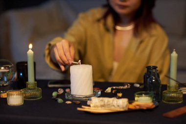 Unrecognizable Asian girl sitting at table, lighting up candle for magic themed party clipart