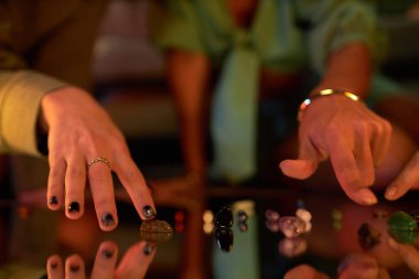 Closeup of hands of unrecognizable girls placing gemstones on mirror surface for fortune telling or spell casting clipart