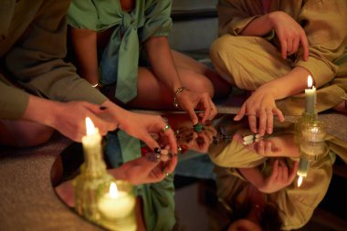 Closeup of unrecognizable young women arranging candles and gemstones on mirror during witchcore party at home clipart