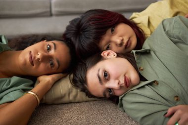 Üç farklı etnik çeşitlilikte rahatlamış kız oturma odasında başlarını yastığa koyup kameraya bakıyorlar.