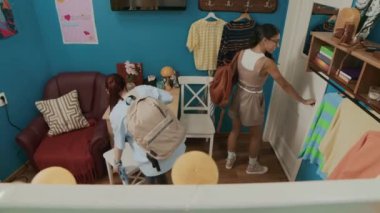 İki üniversite öğrencisinin rahat yurt odasına girerken, kapıyı kapatırken ve dersten sonra çantalarını açarken yüksek açılı görüntüsü var.