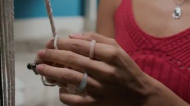 Yüzük takan tanınmayan bir kızın, makrome tekniği kullanarak iç malzemeyi hızla dokuduğu yakın çekim görüntüsü.