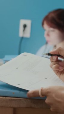 Sınav için hazırlanırken üniversiteli bir kızın ders kitaplarının yanındaki masada matematik ödevi yaptığı dikey yakın çekim. Arka plandaki oda arkadaşı...