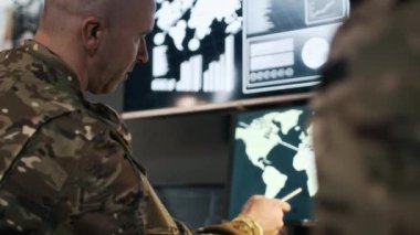 Düşük açı, iki istihbarat ajanının kamuflaj üniformalı yavaşlaması küresel haritada malzeme teslimatını kontrol ederken komuta merkezinde bilgisayar ekranının önünde oturması.