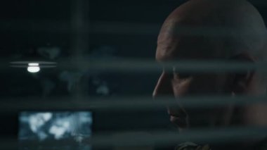 Askeri üniformalı, yorgun, beyaz bir adamın gözlüğünü çıkarıp kumanda merkezindeki panjurlardan bakarken gözlerini dinlendirirken...