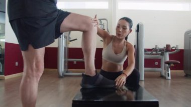 Genç Asyalı kadın antrenör, modern fitness merkezindeki platformda egzersiz yapan adama talimat veriyor.