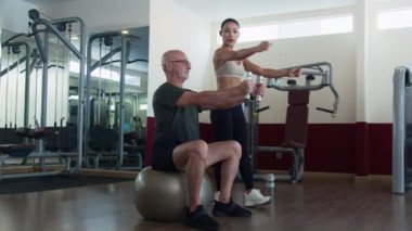 Aktif giyimli beyaz bir adamın spor salonunda bayan Asya koçu antrenman yaparken spor salonunda ağırlık egzersizi yapması çok zor.