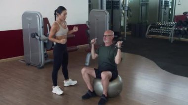 Genç Asyalı eğitmenin spor salonundaki bireysel rehabilitasyon seansında spor topunun üzerinde otururken, halterleri kaldıran olgun beyaz bir adamla iletişim kurma ihtimali çok düşük.