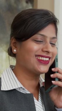 İş yerinde cep telefonuyla konuşan neşeli Hintli kadın çalışanın dikey çekimi.