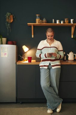 Modern mutfakta dijital tablet kullanan bir kadının portresi. Tabletle uğraşırken gülümsüyor. Arka planda çeşitli mutfak eşyaları, bitkiler ve aletler var.