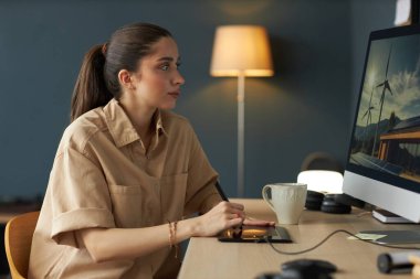 Çağdaş çalışma istasyonunda masa lambası ve kupa kullanan bir kadın. Görüntü odaklanma ve üretkenlik duygusunu çağrıştırıyor