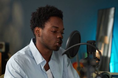 Stüdyoda akustik gitar çalarken mikrofona şarkı söyleyen adam performansa odaklanıyor.