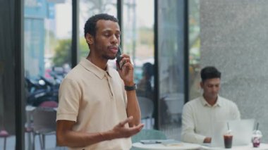 İş arkadaşı kahve molası sırasında arka planda bilgisayarla çalışırken Afro-Amerikan iş adamının cep telefonuyla konuşma fotoğrafı.