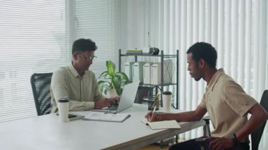 Modern ofiste dizüstü bilgisayarla proje detaylarını tartışan melez erkek arkadaşlarımızın statik görüntüleri.