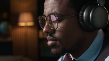 Klasik giyinmiş Afro-Amerikan bir adam iç mekan ortamında kulaklıkla müzik dinliyor.