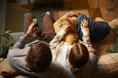 Üst görüntüde aile bireyleri birlikte kanepede dinleniyor, rahat oturma odasında televizyon seyrediyor. Sahne, sevdiklerin arasında sıcak bir bağ kurma anı yakalar