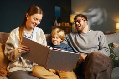 Gülümseyen aile, kitap okurken, kitap okurken, kitap okurken, kitap okurken, ışık okurken, oturma odasında davetkar ve rahat bir atmosfer yaratırken rahat vakit geçirir.