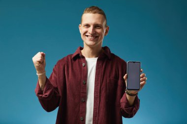 Kafkasyalı genç bir adamın portresi elinde akıllı telefon ve zaferi kutlarken yumruğunu kaldırıp kırmızı gömleğini giyip kameraya bakıyordu.