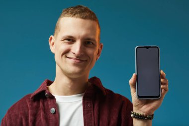 Elinde akıllı bir telefonla kameraya bakan gülümseyen bir adamın portresi.