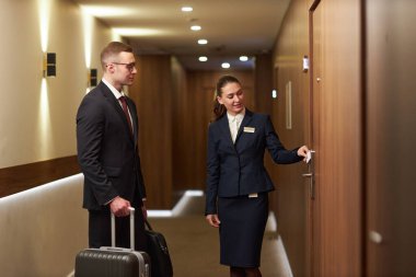 İki iş adamı bir otel odasına giriyor, ellerinde bavullarıyla, iyi aydınlatılmış bir koridorda. İş seyahati ve profesyonelliği öneren mesleki kıyafet ve dengeli davranış
