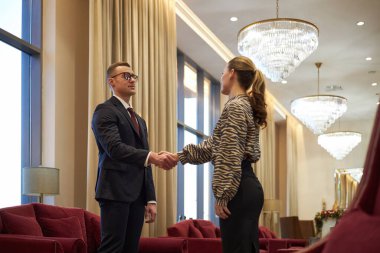 Modern ofiste zarif avizeler ve yumuşak ışıklandırma altında el sıkışan iş adamları başarılı bir anlaşma ve işbirliği sergilediler.