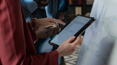 Beyaz bir kadının dijital tablet üzerinde VLM kullanırken Afrikalı Amerikalı bir erkek meslektaşın ofiste yazı yazarken görüntüsünü kaldır.
