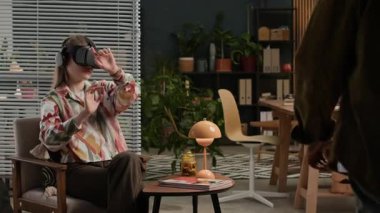 Afrika kökenli Amerikalı erkek iş arkadaşı dijital cihazlardaki kodlama ekranlarıyla masada otururken, beyaz kadın geliştiricinin güçlendirilmiş gerçeklik kulaklığı ile çalışmasının zor bir çekimi.