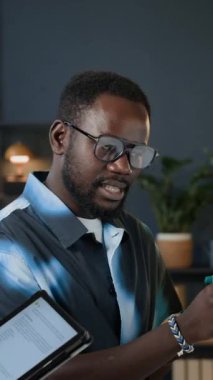 Genç Afrikalı Amerikalı erkek yöneticinin dijital tableti elinde tutan meslektaşıyla çalışma görevlerini tartışırken dikey çekimi