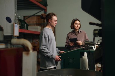 Kafkasyalı genç işçilerin kahve çekirdeklerini profesyonel kızartma makinesinde kızartırken geniş açılı görüntüsü.