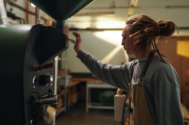 Önlük giymiş genç bir adam büyük bir kızartma makinesinin önünde dikiliyor ve fırlatmak için can sıkıcı bir kol kullanıyor.