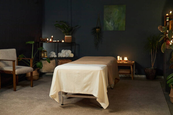 Relaxing massage table setup in a tranquil room setting with candles, plants, and comfortable seating creating a peaceful and soothing atmosphere