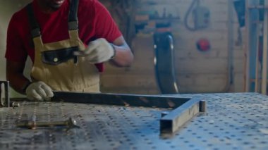 Genç Afro-Amerikan bir adamın fabrikada metal ve ahşapla çalışırken yakın plan çekimi.