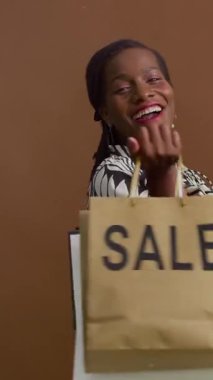 Siyah kadının dikey portresi. Kameraya bakıyor. Gülümsüyor, alışveriş torbalarıyla içeride poz veriyor.