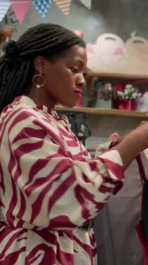 Modern mağazada elbise seçen siyahi bir kadının dikey fotoğrafı.