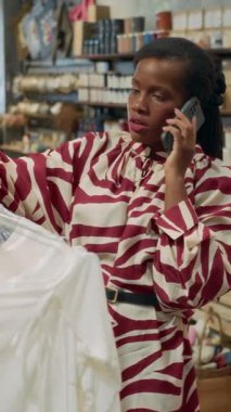 Zarif elbiseli siyahi kadın müşterinin alışveriş merkezini ziyaret ederken akıllı telefondan konuştuğu dikey bir fotoğraf.