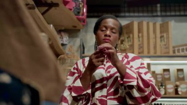 Zarif bluz giymiş genç Afro-Amerikan bayan müşterinin düşük açılı görüntüsü mağazadaki kokuyu test ediyor