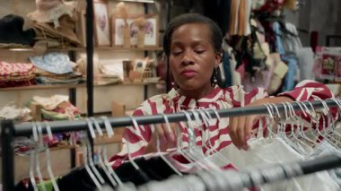 Afro-Amerikalı bir kadının moda mağazasında elbise seçerken orta boy fotoğrafı.