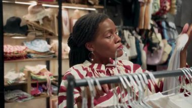 Siyahi bir bayanın moda butikte iki elbise arasında seçim yaptığı orta ölçekli yakın çekim.